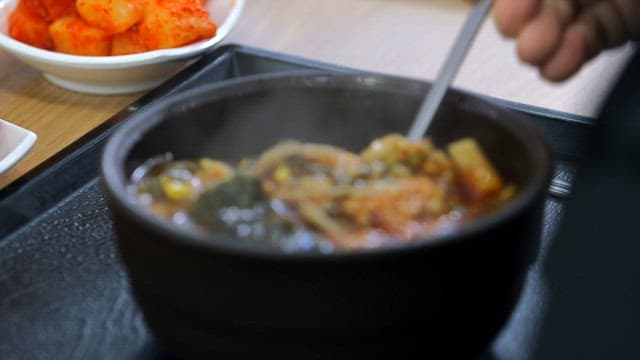 Mixing hot and spicy Korean beef soup with spoon