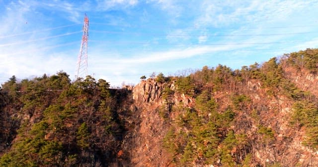 나무가 많은 산 위 절벽에 위치한 송전탑