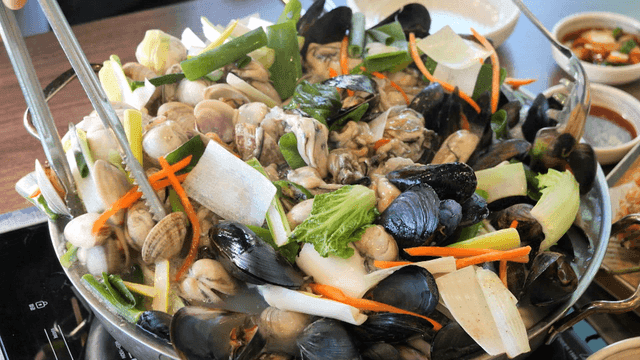 Pot containing oyster kalguksu topped with fresh seafood and vegetables