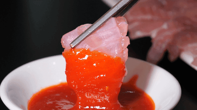Chopsticks dipping skate sashimi into spicy gochujang sauce