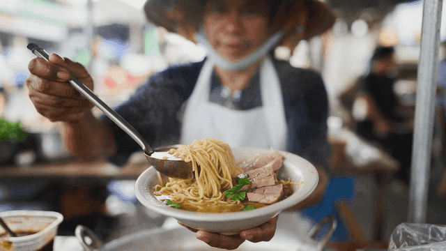 Thai street vendor putting hot noodles into bowl
