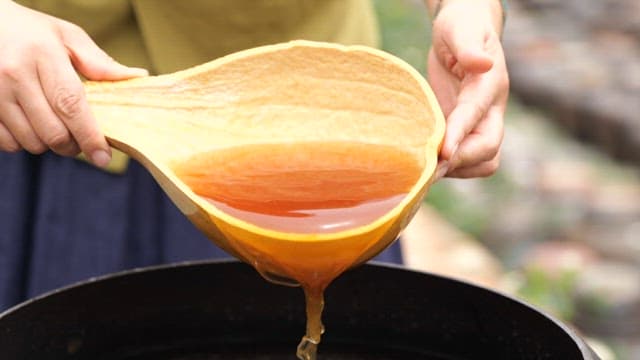 Pouring soy sauce intp a crock jar with a wooden ladle