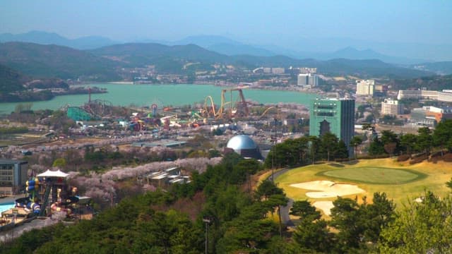 Panoramic view of a lakeside city with amusement park and surrounding mountains