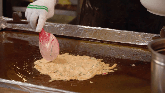 Mung bean pancake dough is spread on griddle.