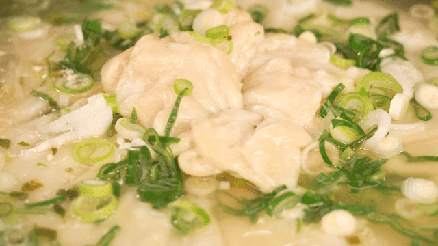 Hearty dumpling soup boiling with green onions