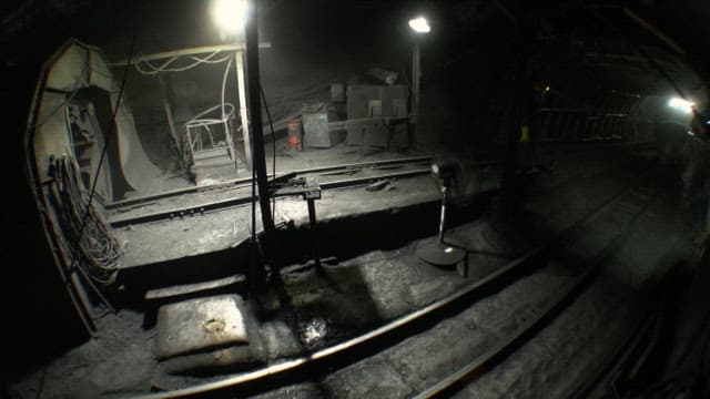 Workers in an underground mine transporting materials in dim lighting.