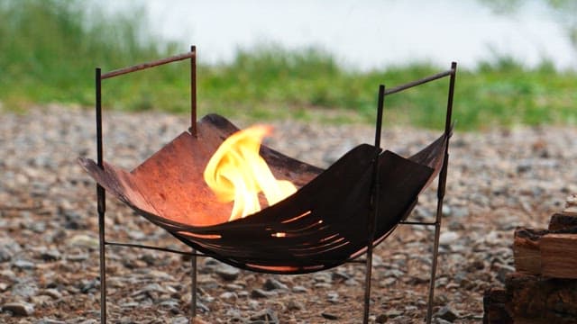 Campfire made of firewood in a brazier on a gravel field