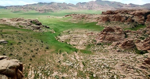 Expansive green plains with rocky mountains