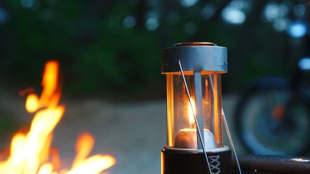 Lantern glowing beside a campfire in a forest