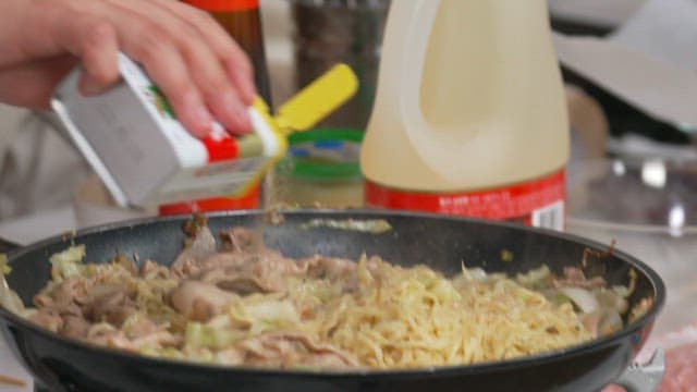 Adding pepper to cooking meat and noodles in frying pan