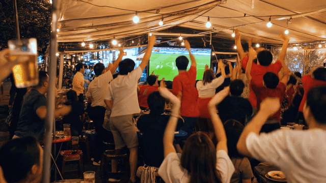 People cheering while watching soccer match at street food stall