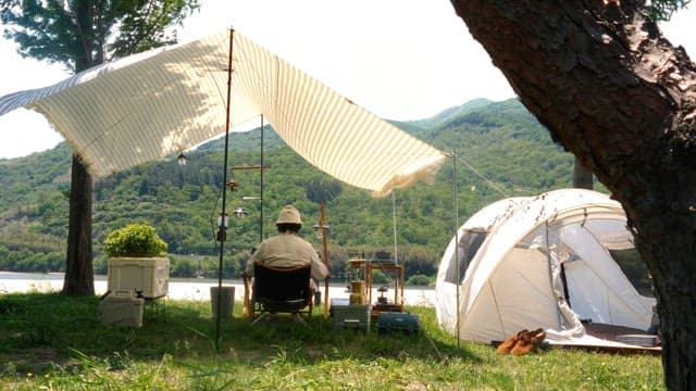 Person relaxing at a riverside campsite during a sunny day