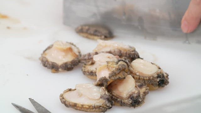 하얀 도마 위에서 칼로 전복을 써는 모습