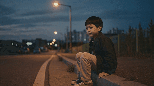 Boy sitting on curb on night road
