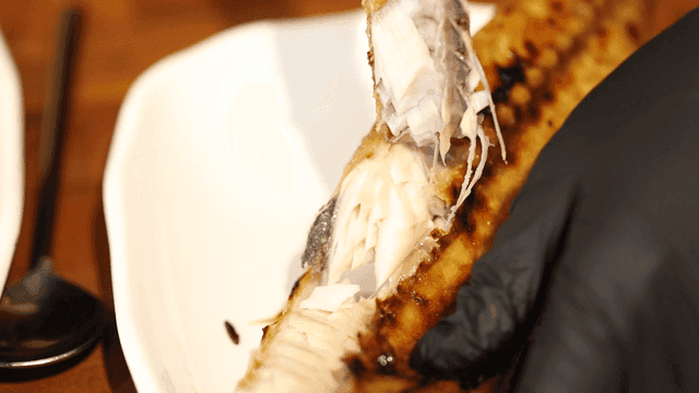 Hands deboning grilled fish on plate