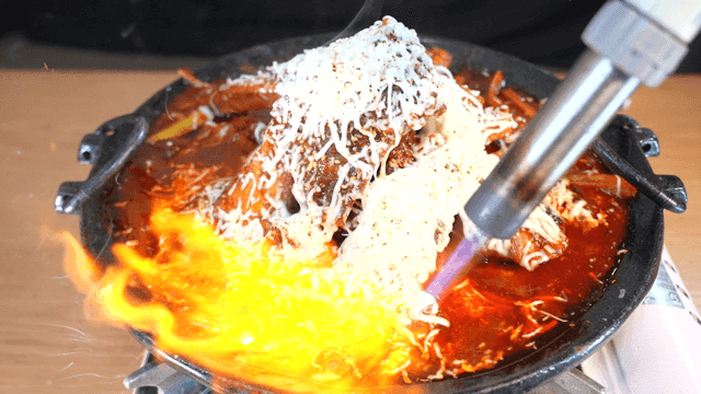 Torch grilling spicy braised short ribs covered in cheese