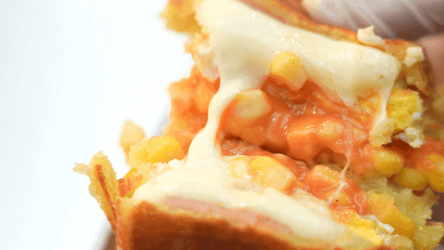 Hand holding cheese and corn sandwich