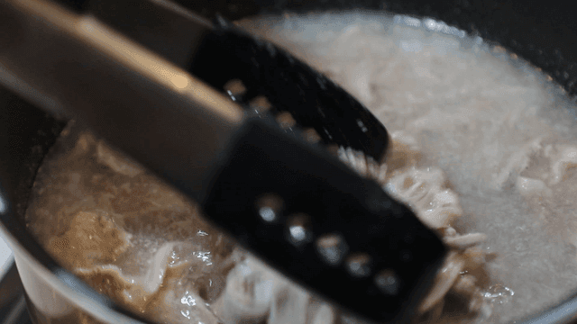 Stirring boiling meat in pot with tongs