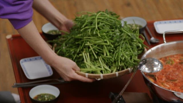 Hands placing a basket containing well-prepared water parsley on a wooden table