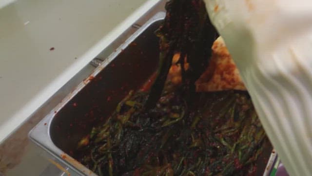 Fresh leaf mustard kimchi being moved on a conveyor belt in a food processing facility