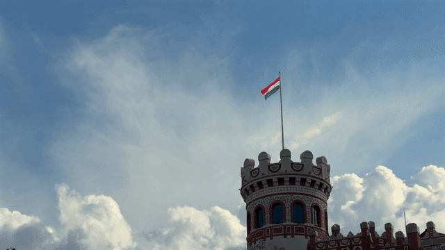 Historic tower with Hungarian flag under blue sky
