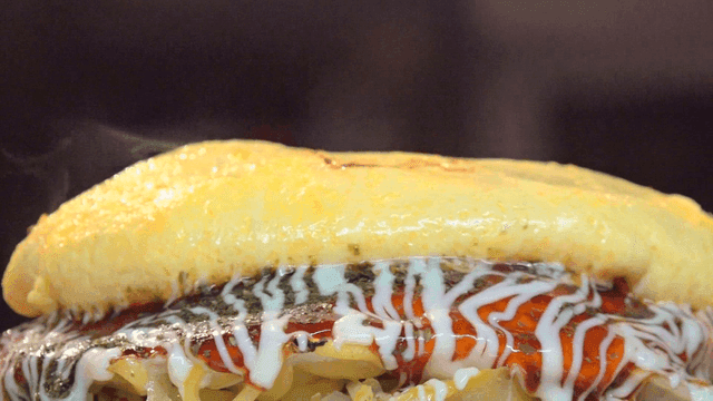 Hot okonomiyaki topped with egg omelet, sauce, and mayonnaise