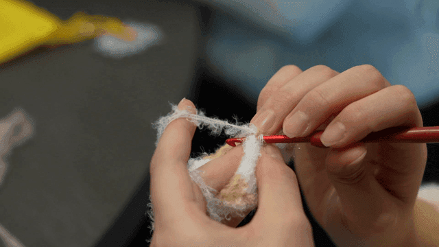 Hands crocheting with a red hook