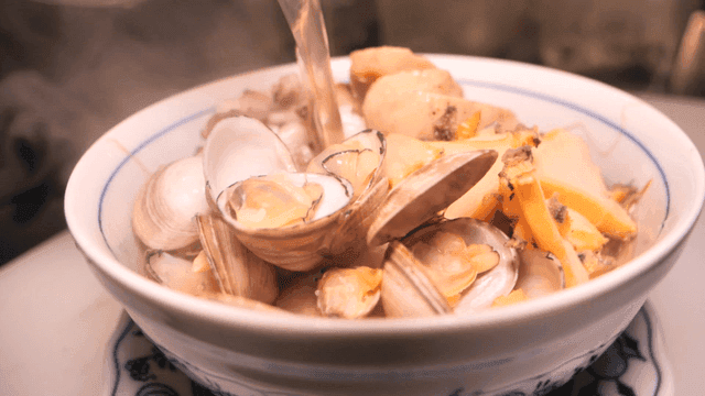Broth poured over seafood rice noodles being prepared in kitchen