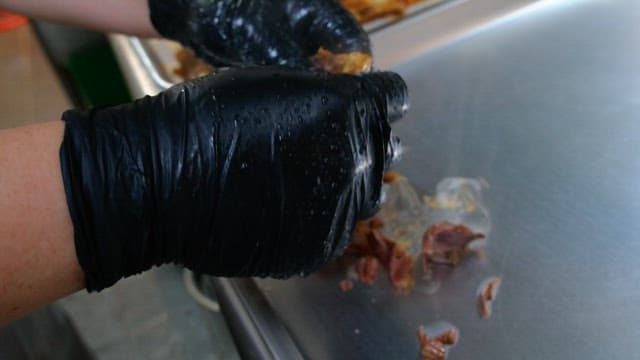 Preparing boiled meat on a metal tray with gloved hands