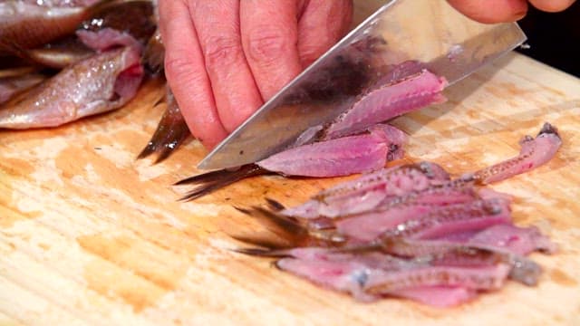 Slicing fresh damselfish on a wooden cutting board