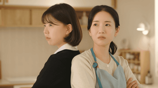 Mother and daughter standing back to back at home