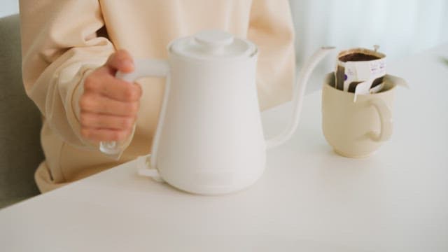 Woman pouring water into cup with coffee pot on table