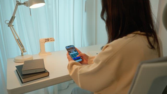 Woman using a smartphone at a desk in a calmly lit room