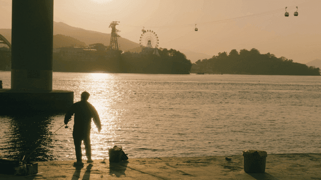 People fishing on riverbank at sunset and cable car