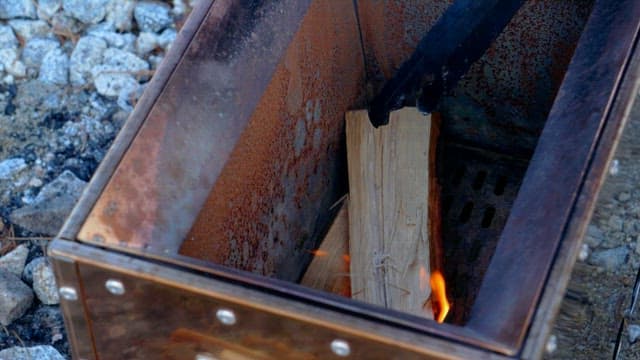 장작과 집게로 금속 화로에 불을 붙이는 장면