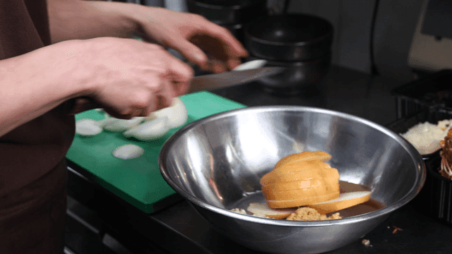 Chef putting chopped onions and pears into bowl in kitchen