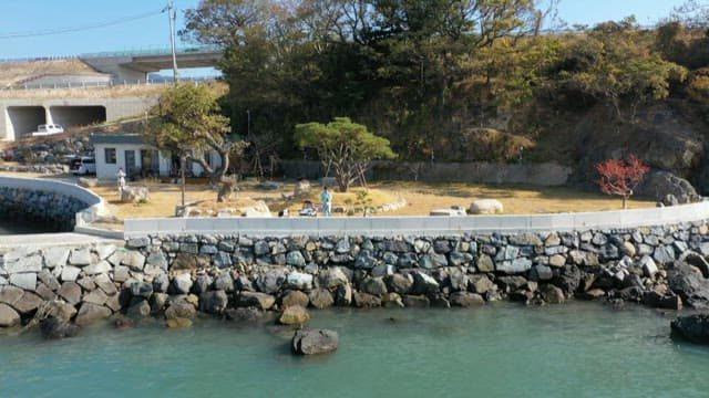 Man fishing on the beach with a small house and trees