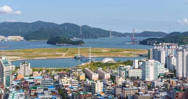 낮부터 밤까지의 하늘 아래 건물과 산, 바다가 있는 도시 경관