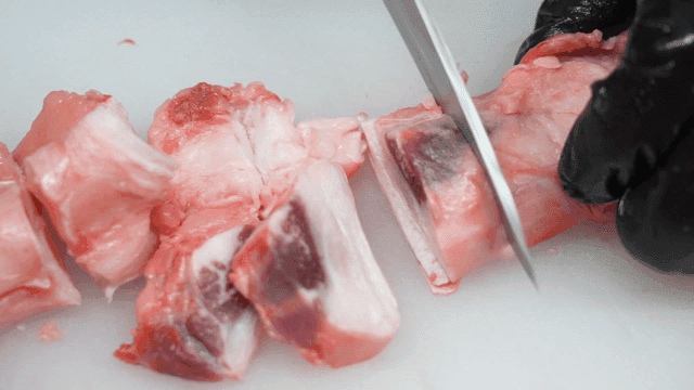 Knife trimming beef tendon on cutting board