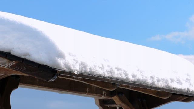 Snow-covered roof of a wooden structure under a bright blue sky