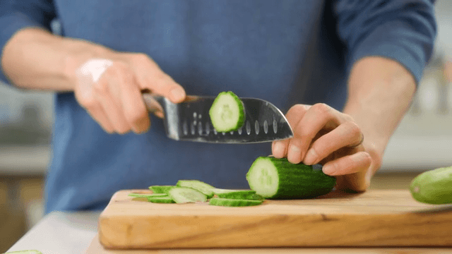 Slicing cucumber on a wooden cutting board