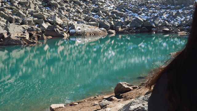 Woman's back view looking at clear lake surrounded by rocks.