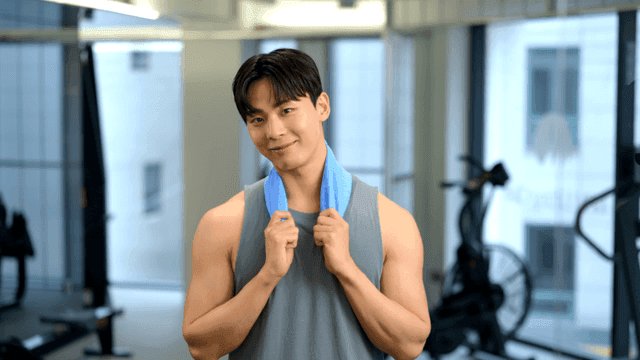 체육관에서 수건을 목에 두르고 정면을 보고 미소짓는 젊은 남자