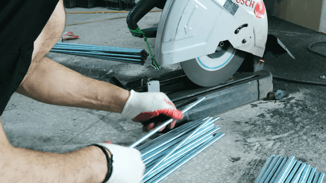 Worker trimming metal rod with electric saw