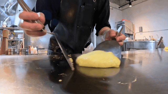 Skilled chef preparing egg omelet on griddle with stone-weighted arm