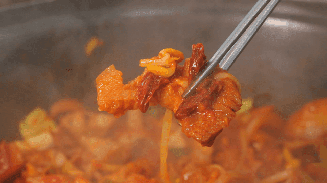 Chopsticks picking up spicy stir-fried pork with pork and vegetables