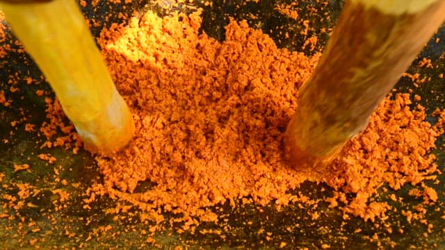 Orange powder being crushed by wooden mortar