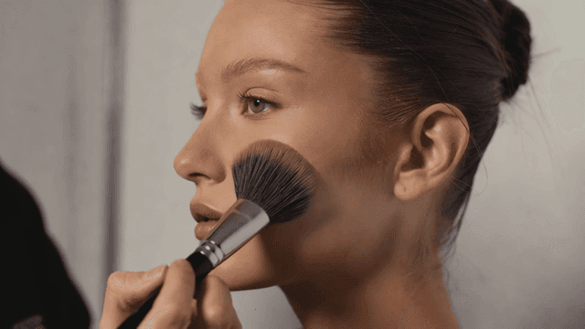 White woman applying blush to model as makeup artist