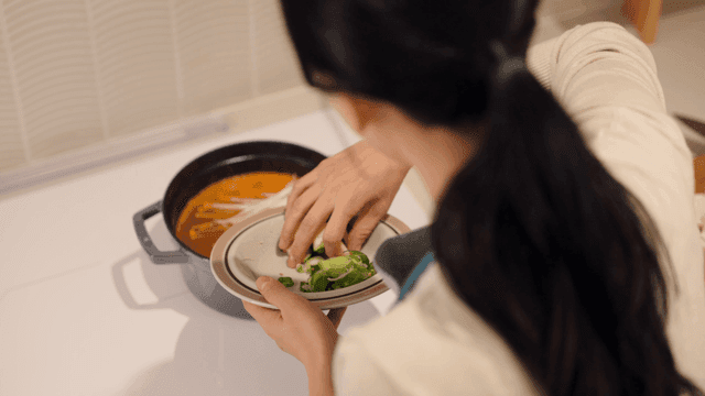 Back view of woman putting vegetables into stew pot