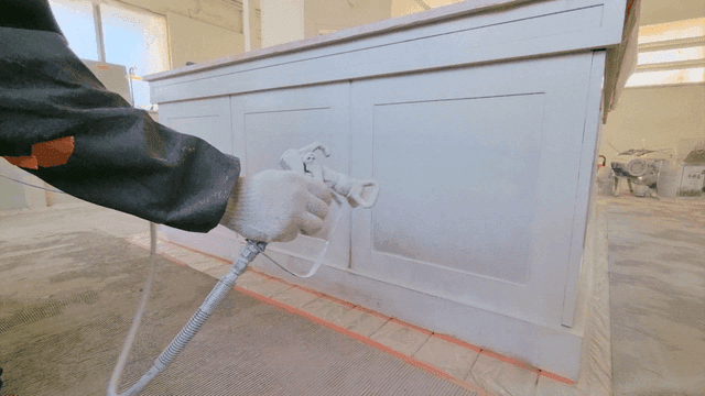 Worker painting wooden furniture with a spray gun